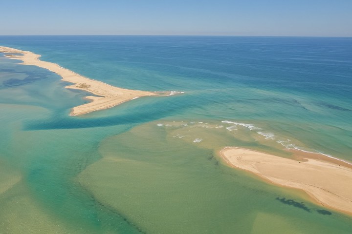 Aerial view of a sandy beach strip with clear turquoise water extending into the ocean.